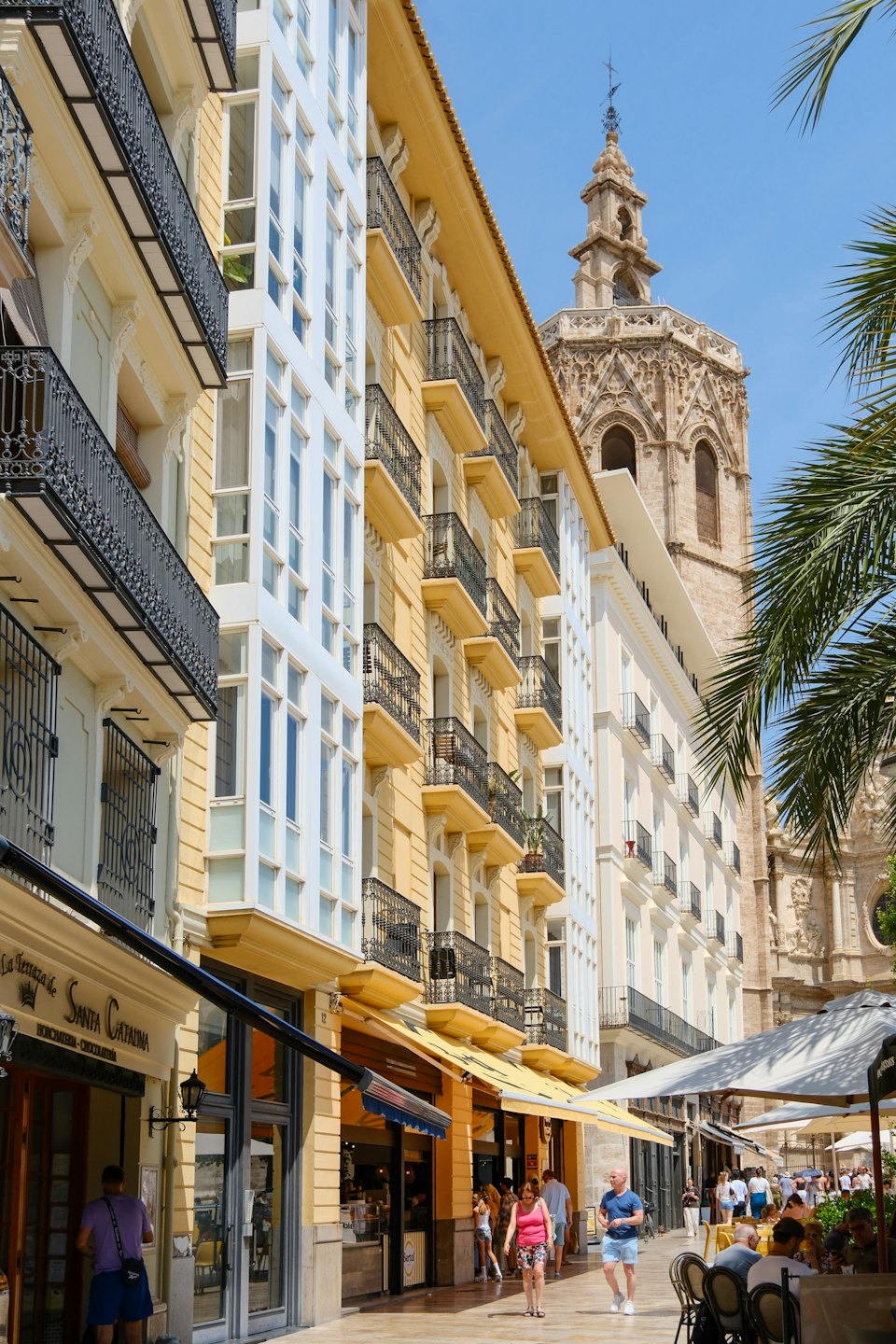 Pedestrians walk past outdoor cafes along a historic city street.